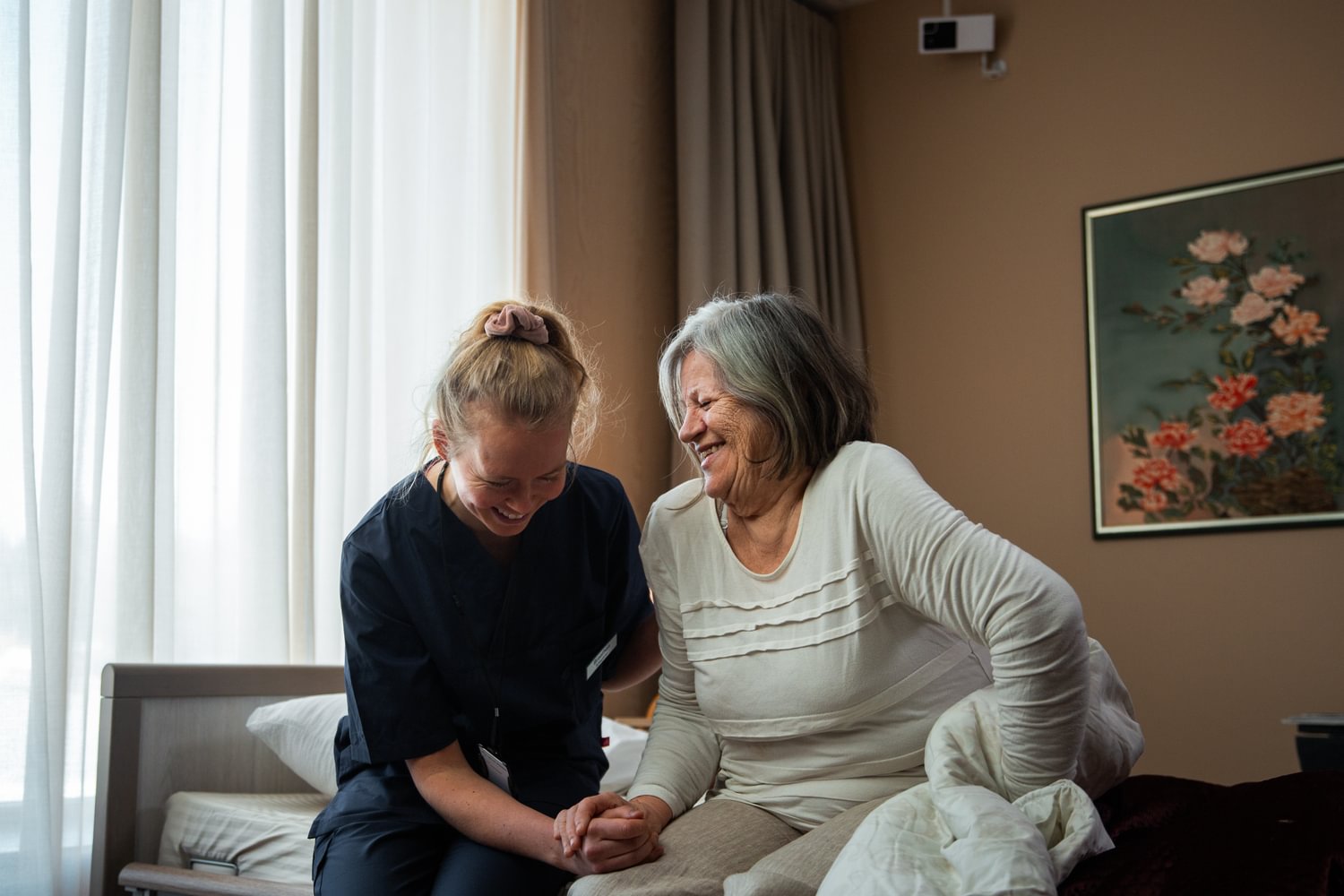 Nurse and resident laughing together. Sensio RoomMate in the background.